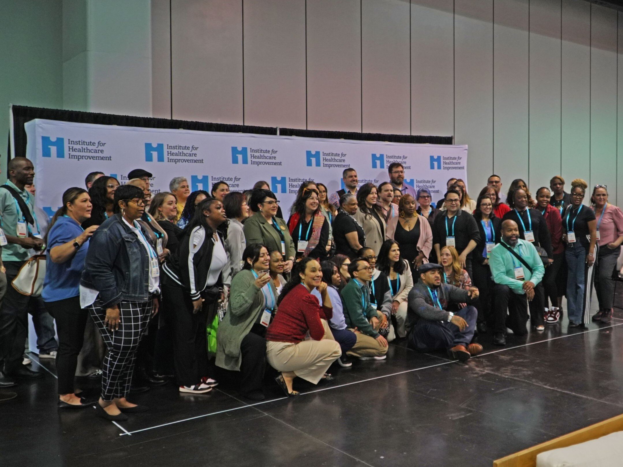 A large group of attendees taking a photo in front of an IHI banner.