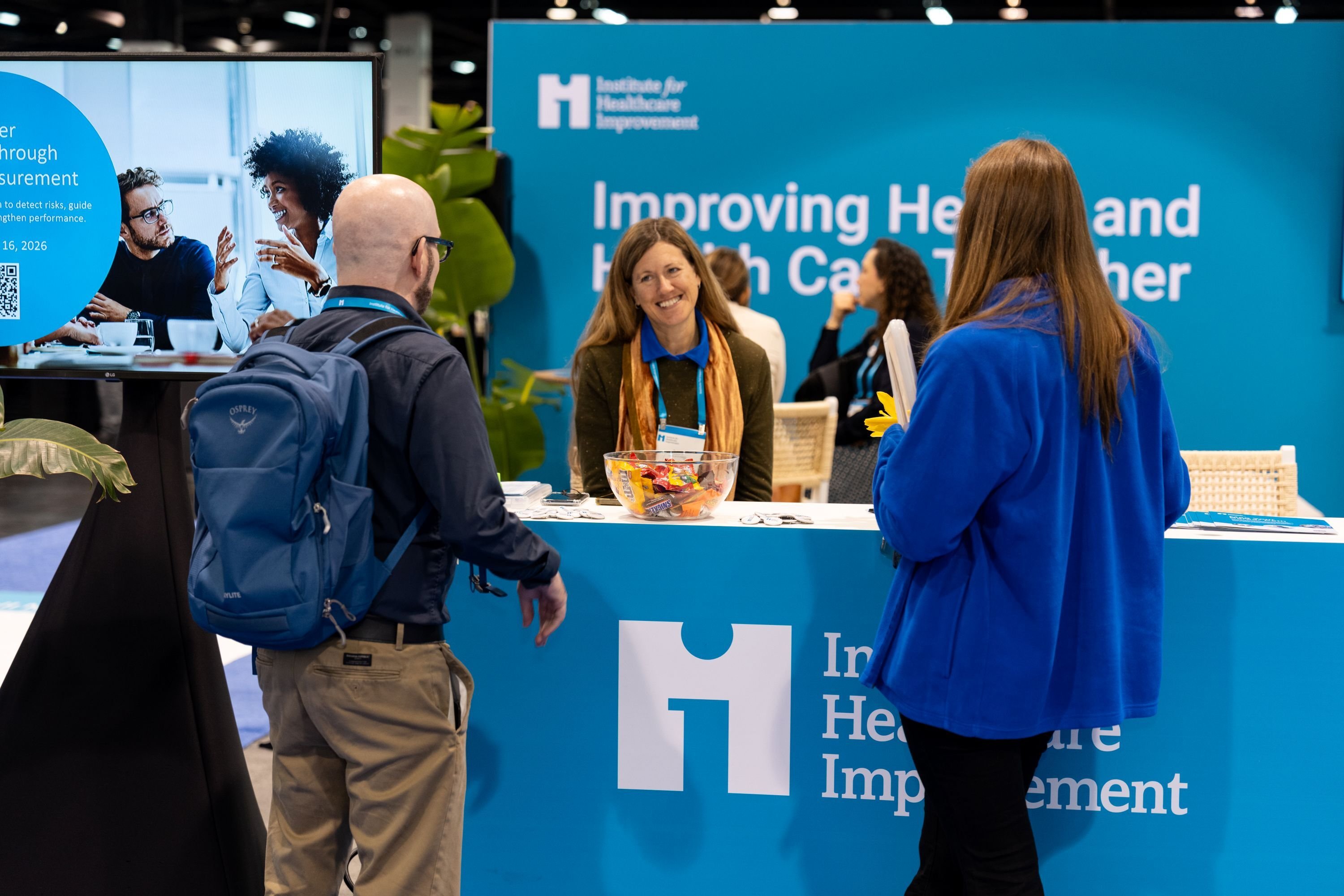 Forum 2025 IHI staff member smiling with 2 attendees at the IHI booth