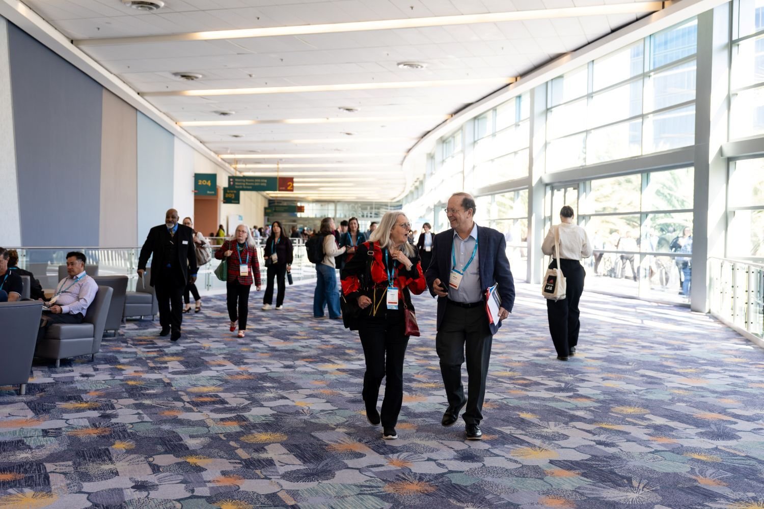 A crowd of attendees walking through a sunny walkway.