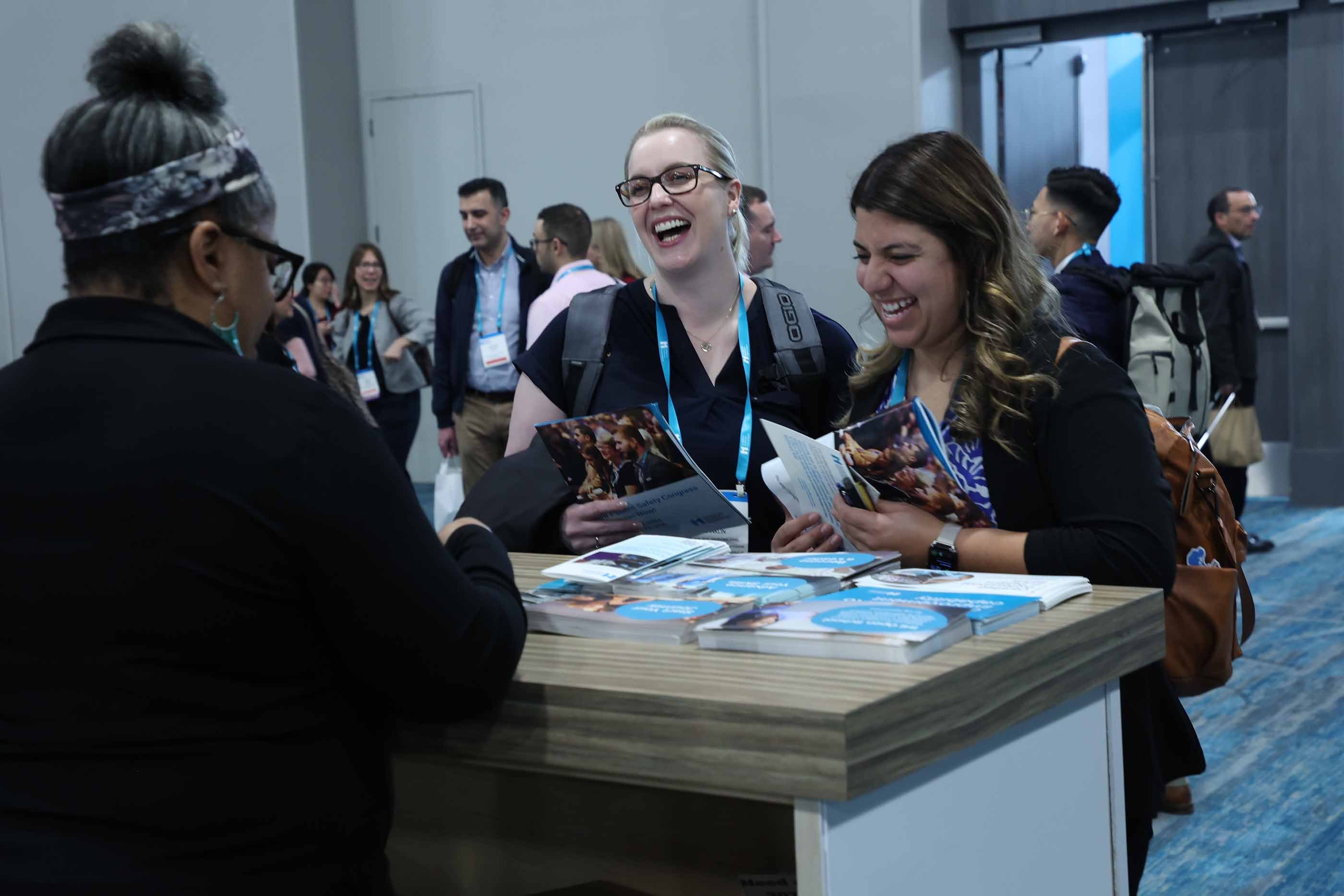 2 attendees smiling while talking to a staff member in the Forum hall.