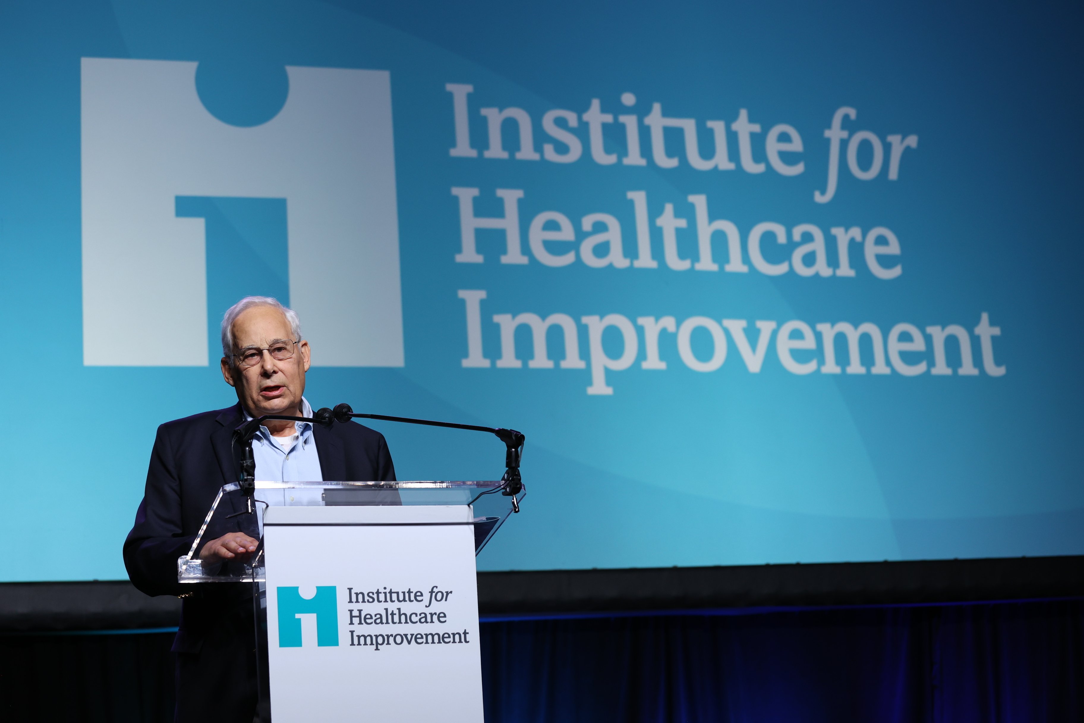Dr. Don Berwick speaking at an IHI-branded podium during a conference.